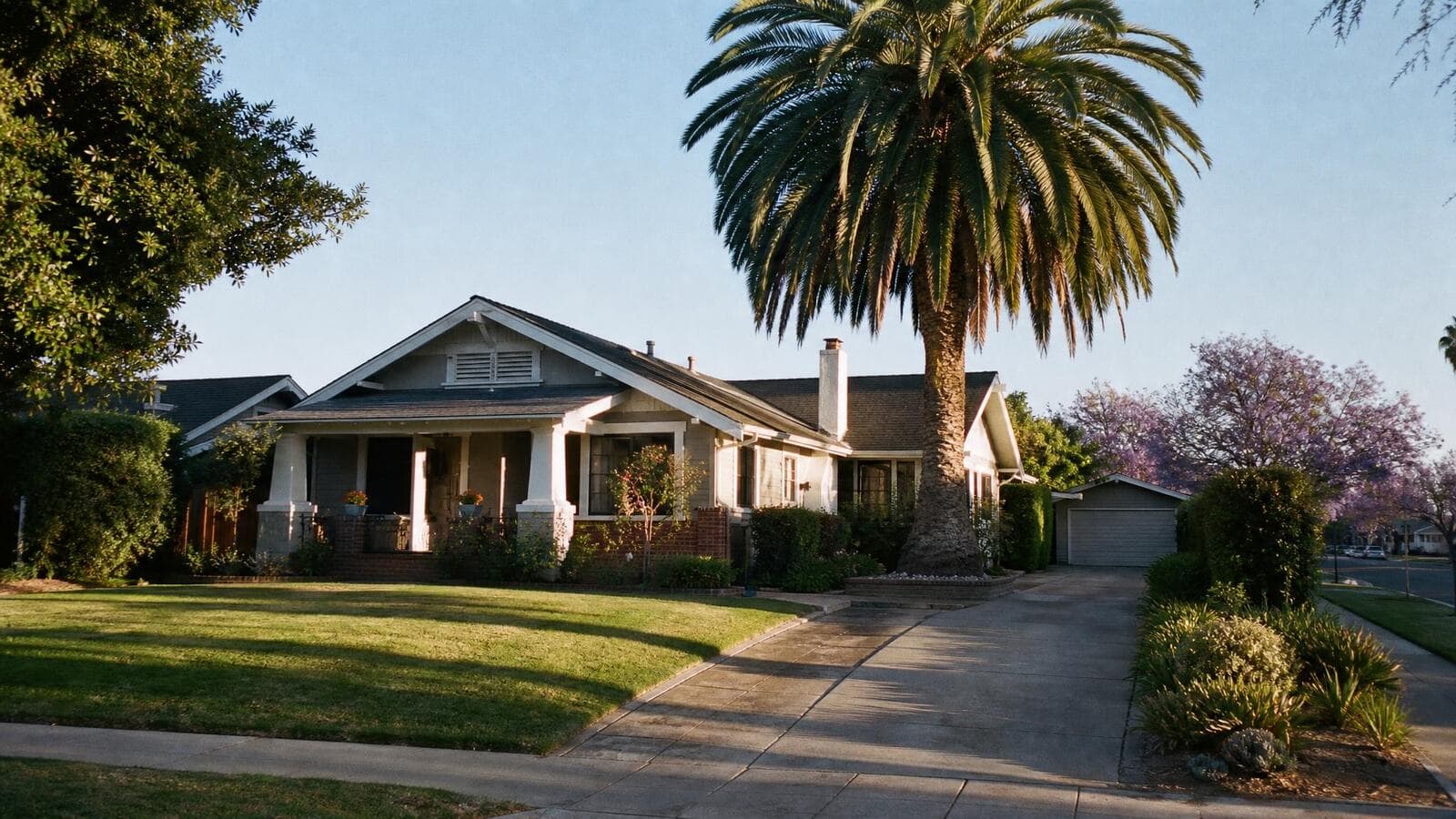 A tidy single-story California bungalow with a wide porch and a mature palm in clear morning light.