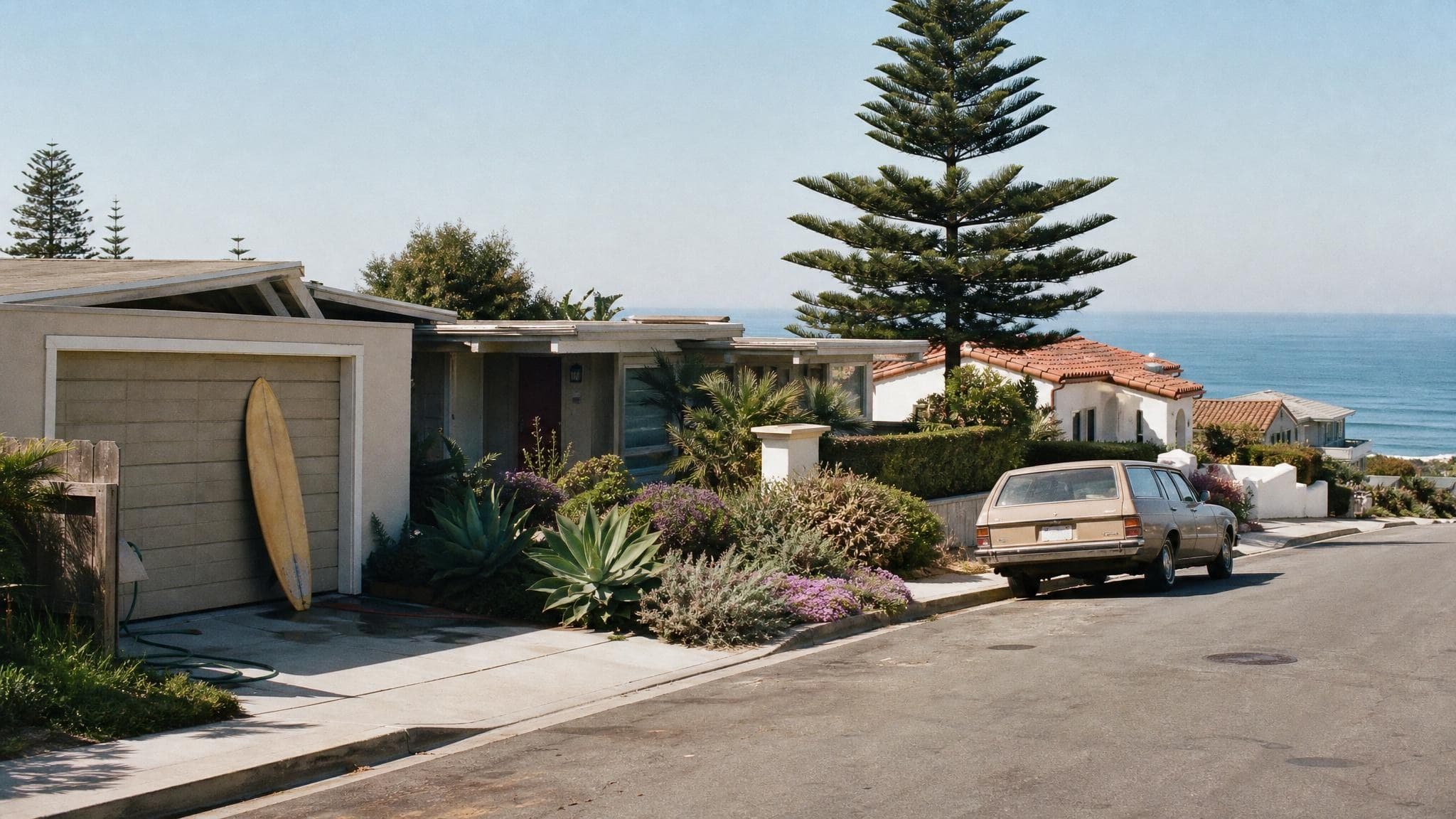 A coastal Point Loma street in San Diego on a bright morning, with a mid-century home, a surfboard by the garage, and the Pacific Ocean beyond the bluff.